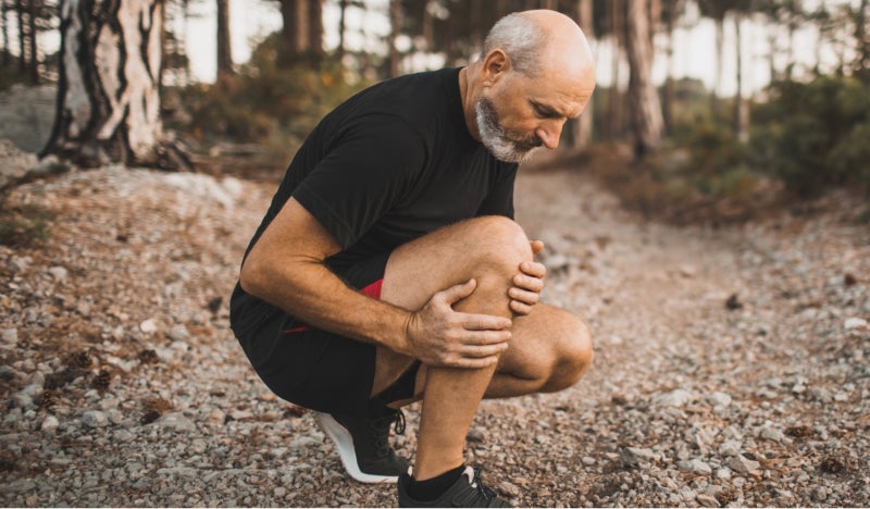 Mature jogging male holding his knee in pain